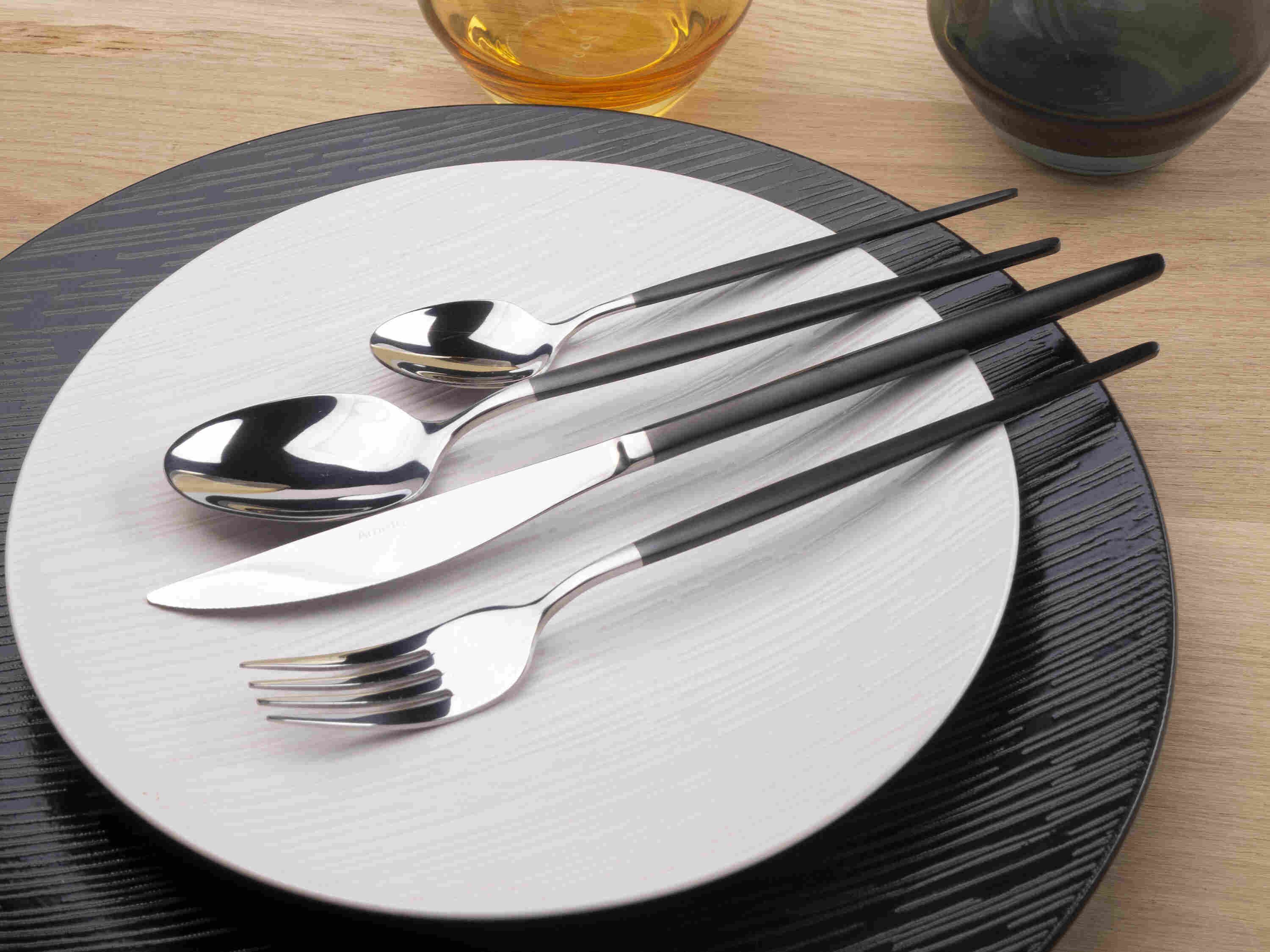 Plan rapproché sur une assiette en porcelaine blanche légèrement striée et ses couverts assortis : une fourchette, un couteau et deux cuillères.