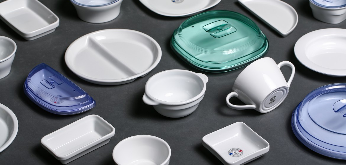 Divers récipients (tasses, bols, plats...) de cuisine disposés sur un grand plan de travail. Certains sont en porcelaine, d'autres en plastiques.