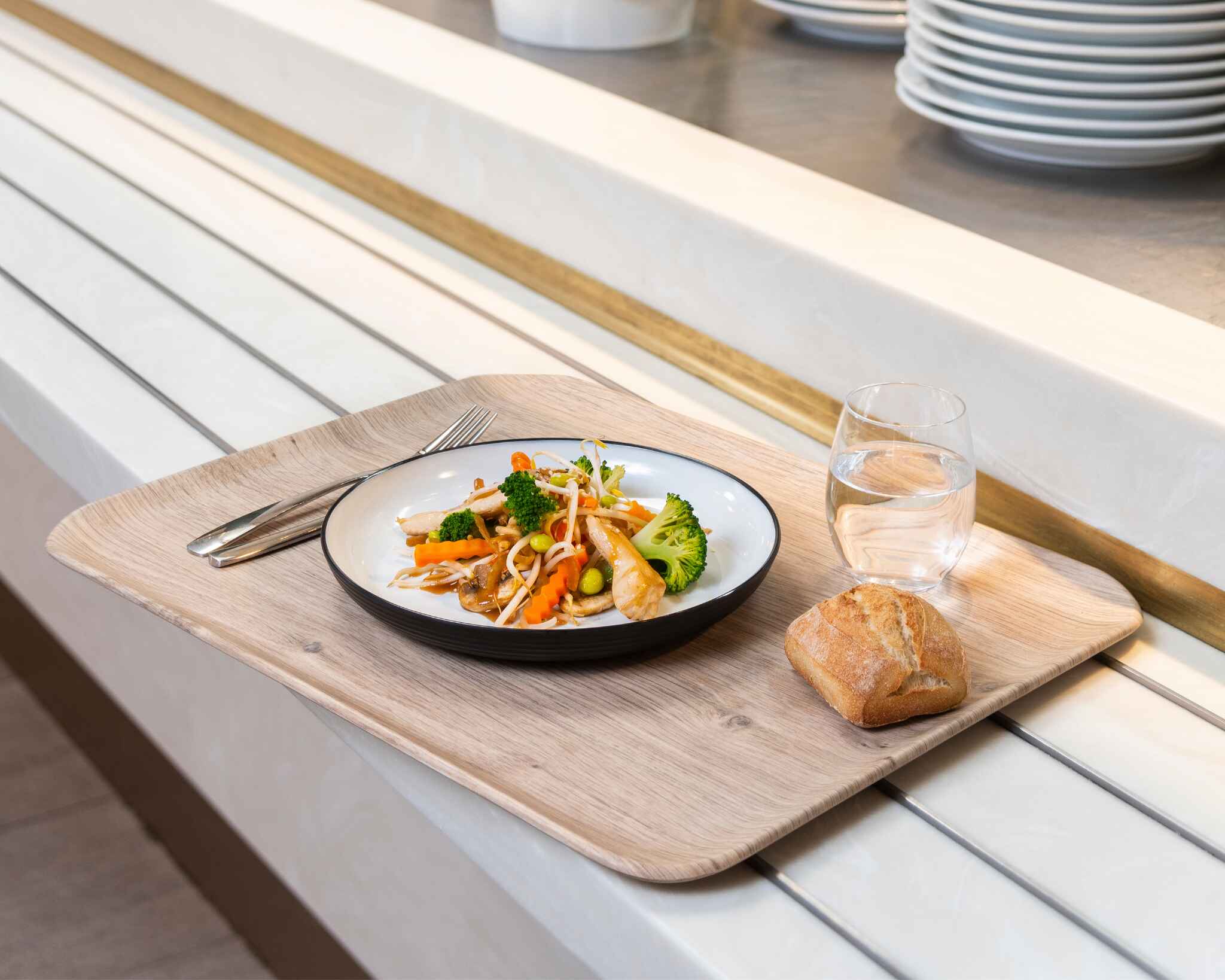 Plateau de cantine contenant un verre d'eau, une tranche de pain et une assiette en porcelaine remplie de légumes.