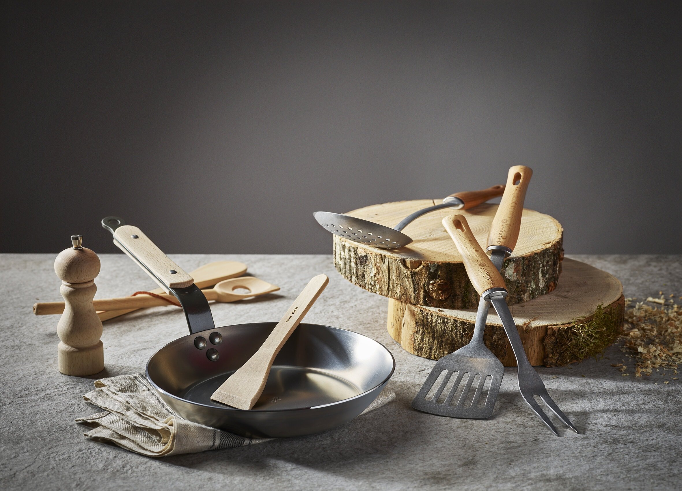 Divers ustensiles (poêle, moulin à poivre...) professionnels de cuisine en bois et inox de la marque De Buyer.
