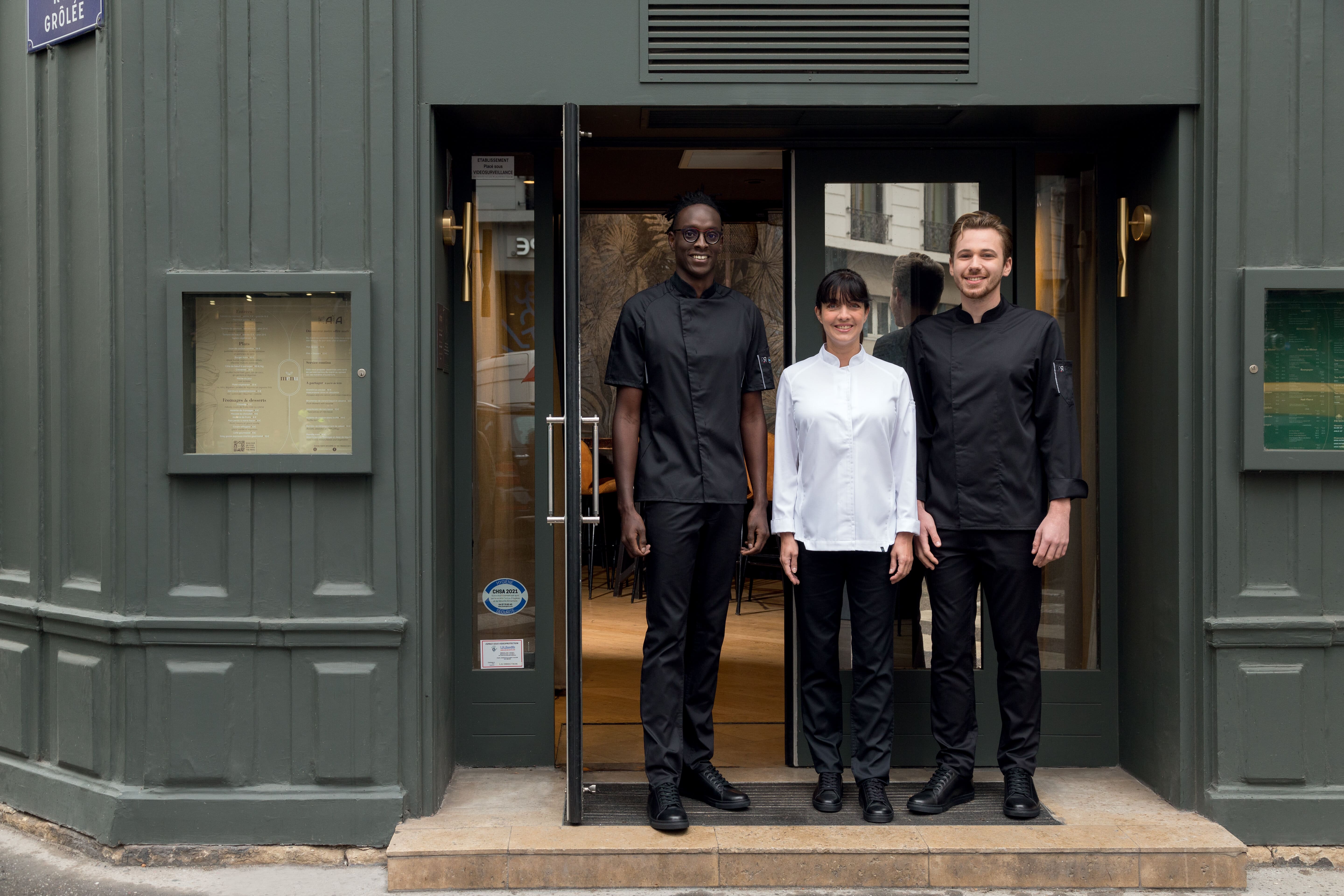 L'équipe d'un restaurant devant la porte de celui-ci : deux hommes et une femme vêtus de vêtements de la marque Robur.